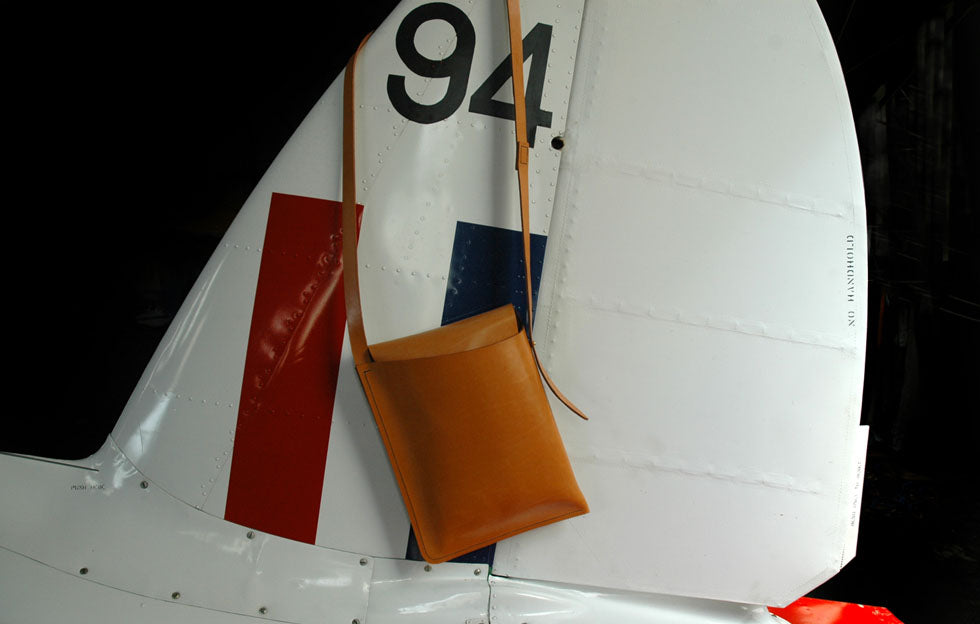 Satchel bag in beige leather sits on the tail fin of a vintage aircraft. The Satchel Bag is from the early collections of Artisan Garvan de Bruir.