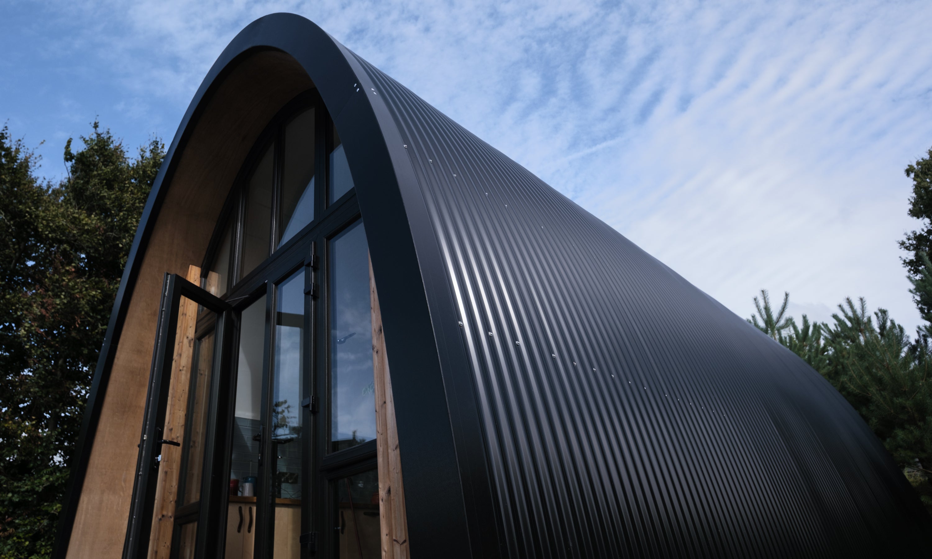 Modern prefab construction for contemporary garden home. Timber frame with curved roof and feature glazing.