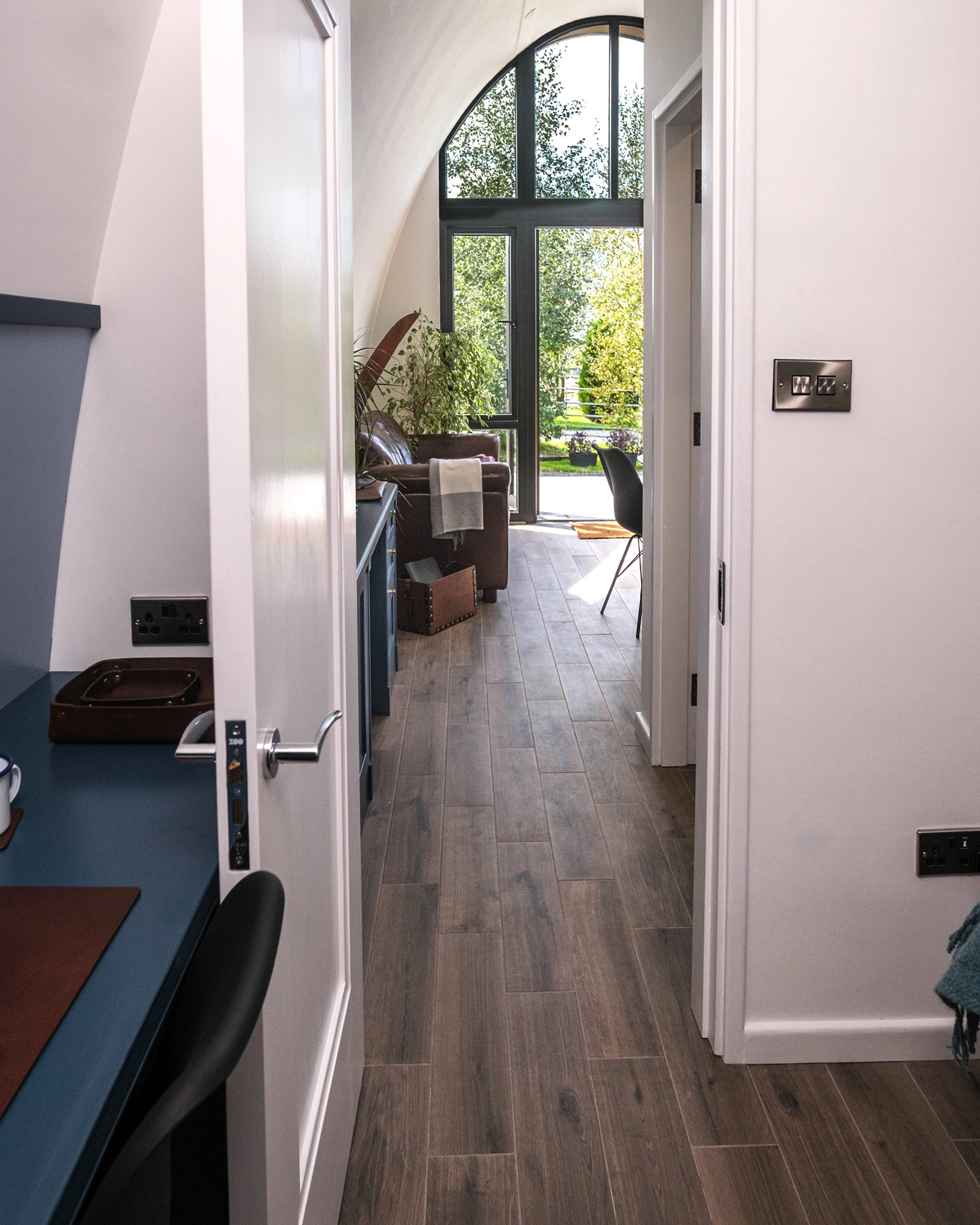 View from the bedroom of the Aviator Lodge showing the hall with bathroom door and office desk, continuing to the sofa area and dramatic front window.