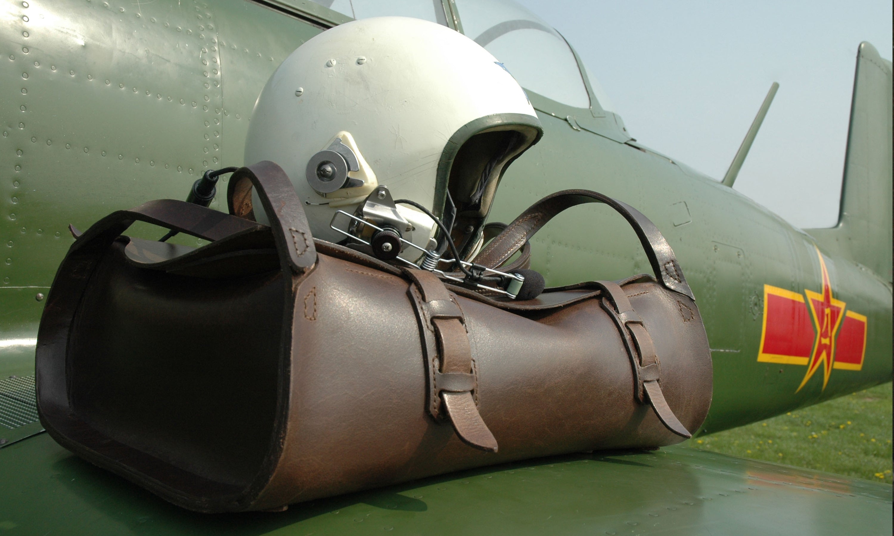 The Parachuter Backpack sits on the wing on a vintage aircraft. A pilots helmet rests on top of the pilots bag.