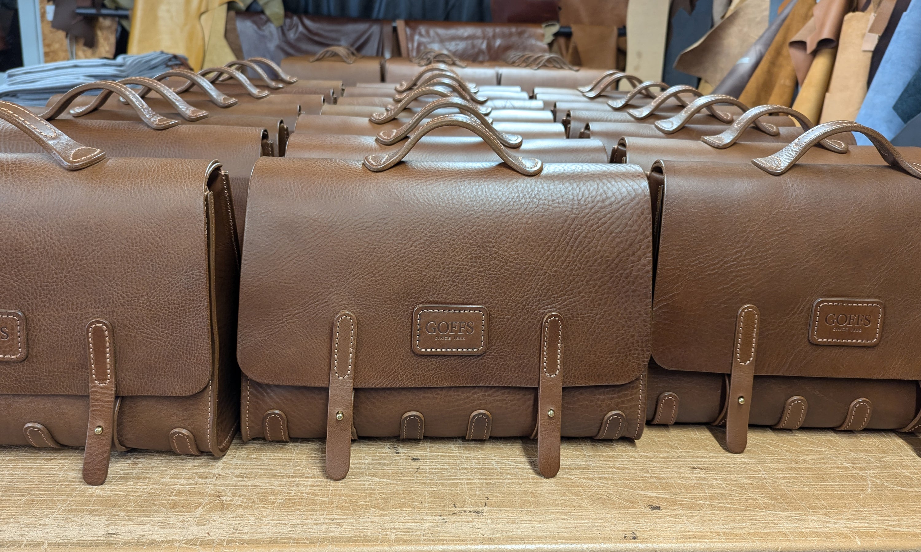 Row of brown leather bags with embossed GOFFS brand name in leather workshop