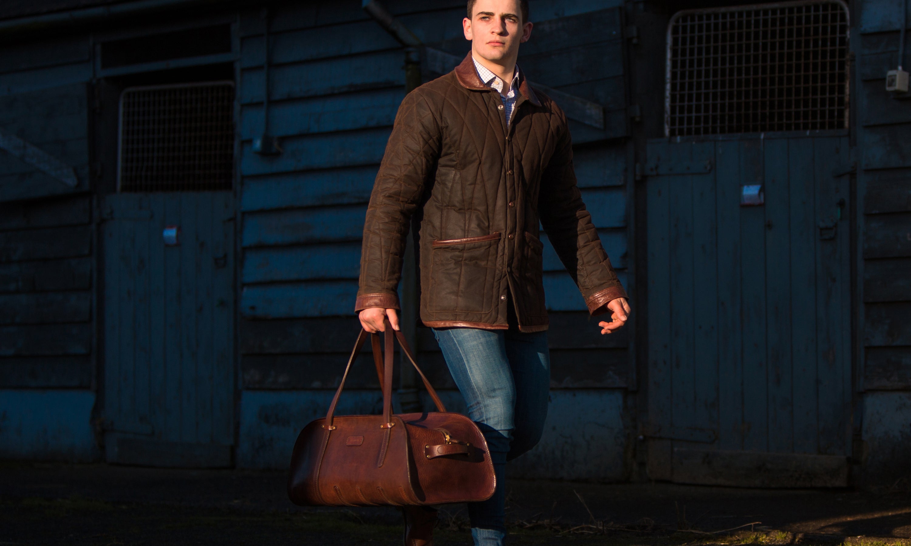 Wax cotton coat with leather details by Garvan de Bruir. Classic country and equestrian outerwear. 
Carrying a Sports Bag.